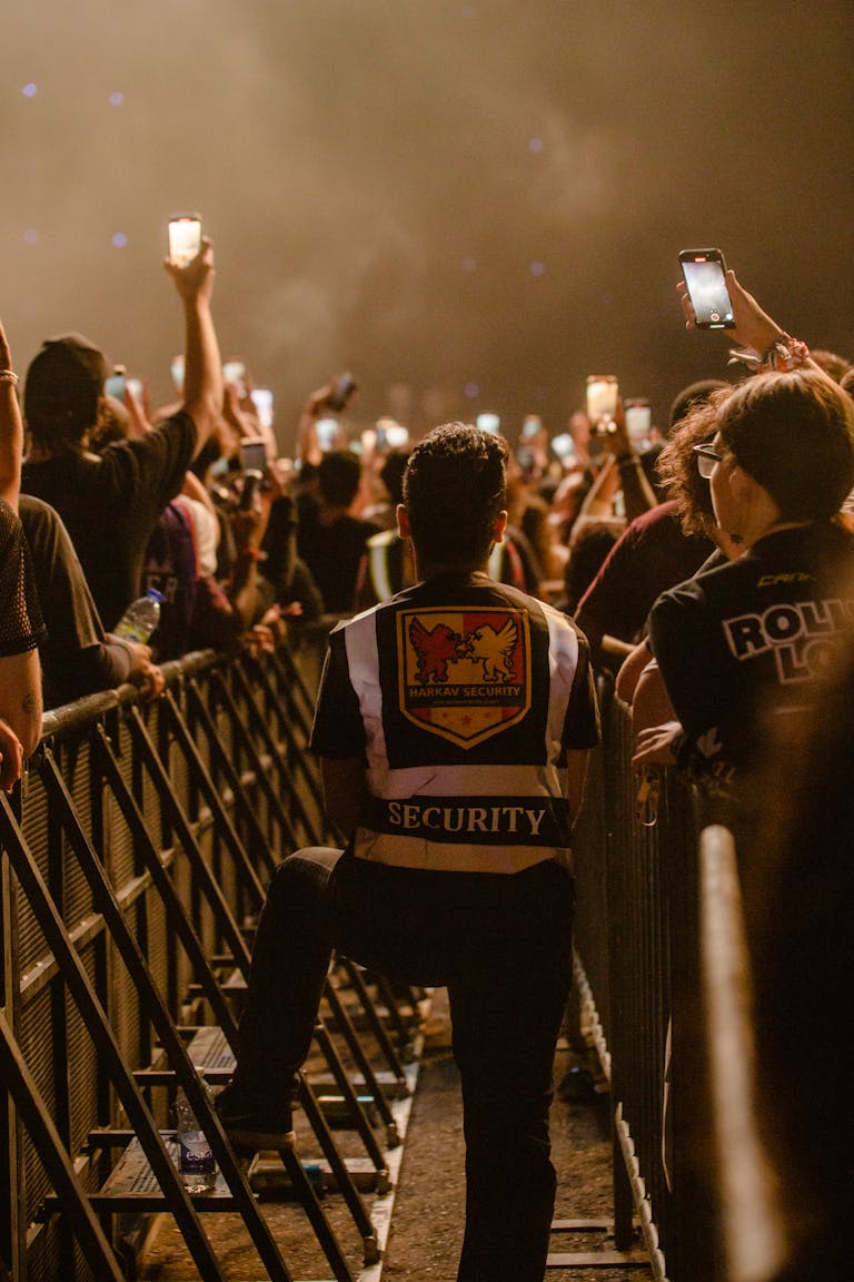 Security guard monitoring a lively concert crowd with smart phones at night.